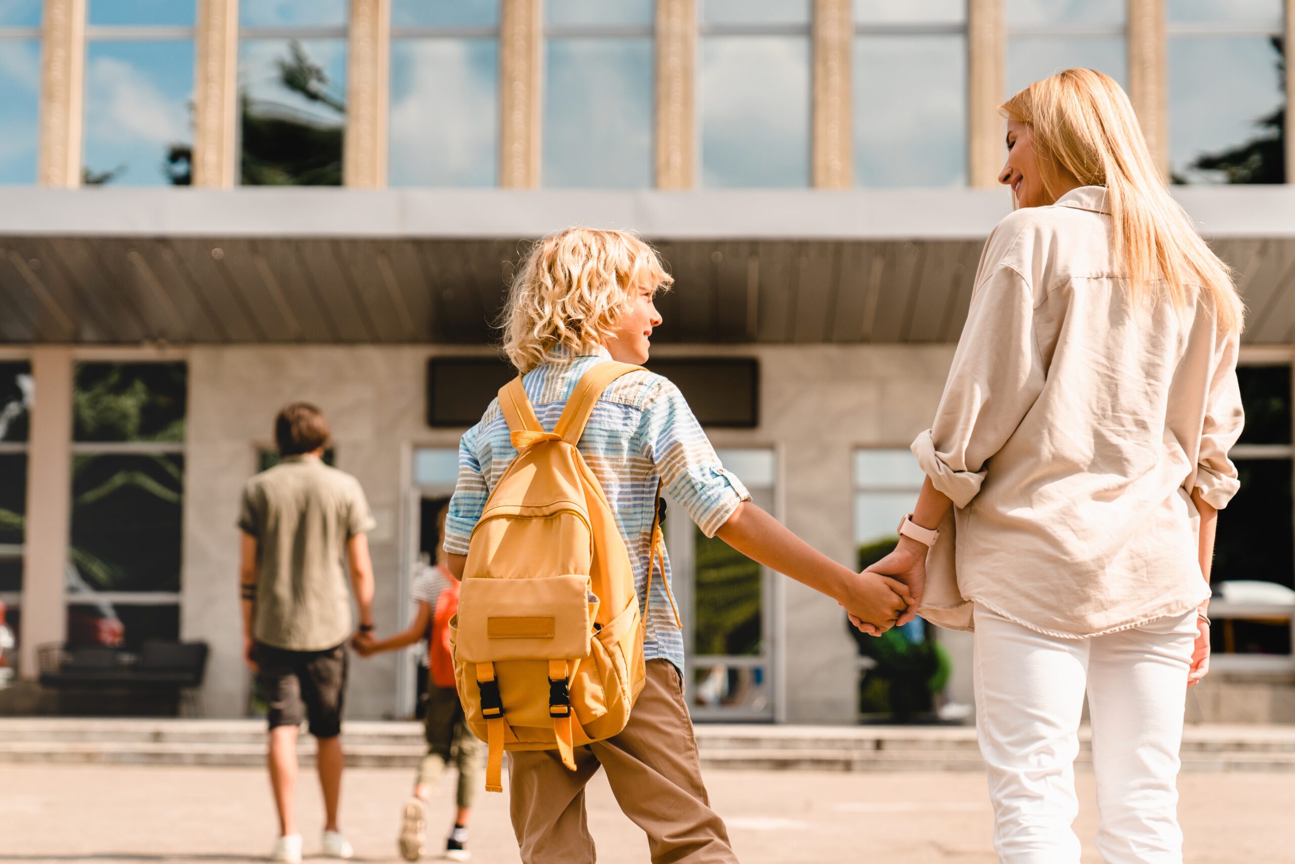 A child with a bright yellow backpack holding hands with an adult—capturing the powerful impact of small beginnings and everyday steps forward.