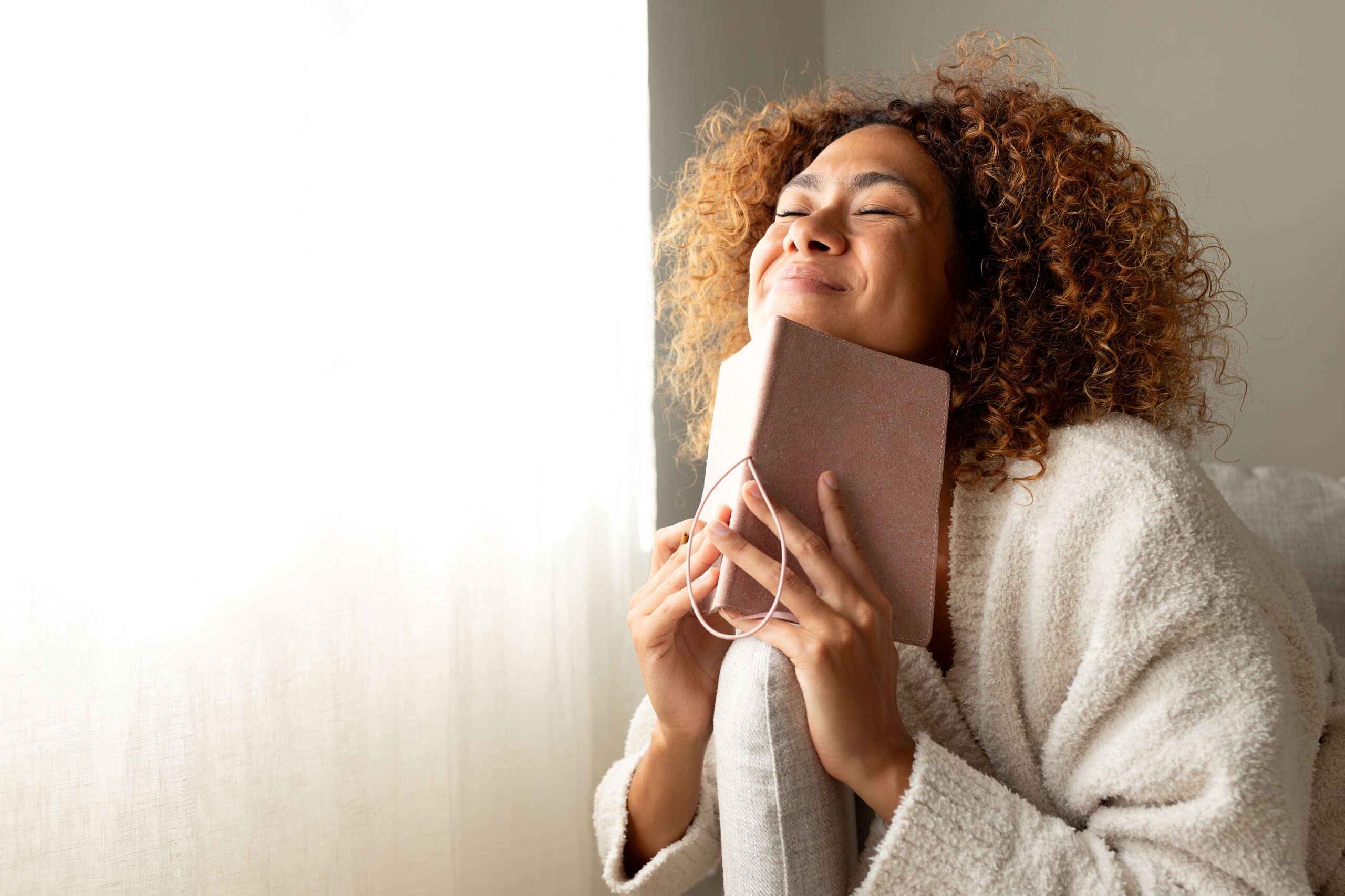 A joyful woman in a cozy robe holding a journal close to her face—capturing the warmth and ease of collecting ideas in an inspiration notebook.