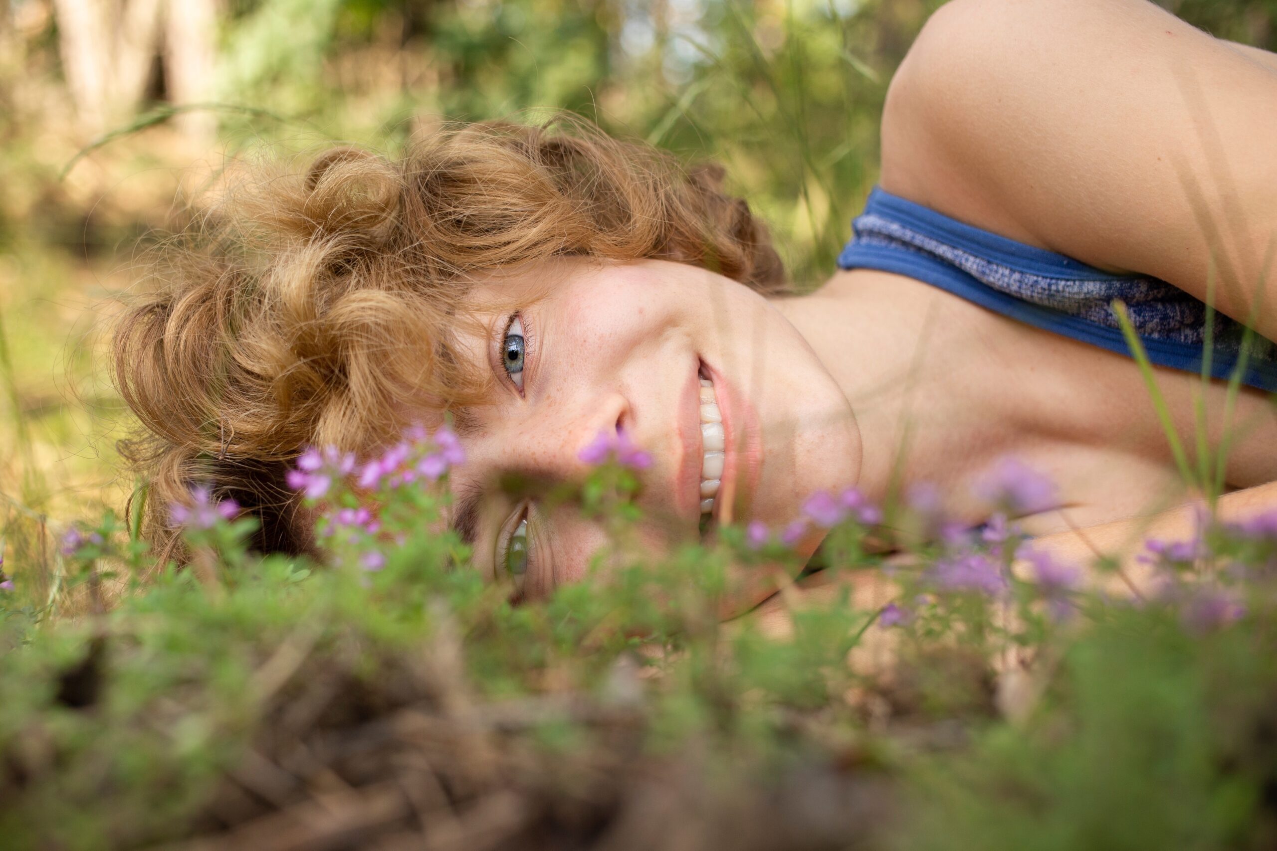 A smiling woman lying in the grass surrounded by wildflowers—symbolizing a grounded, present moment before outside input takes over.