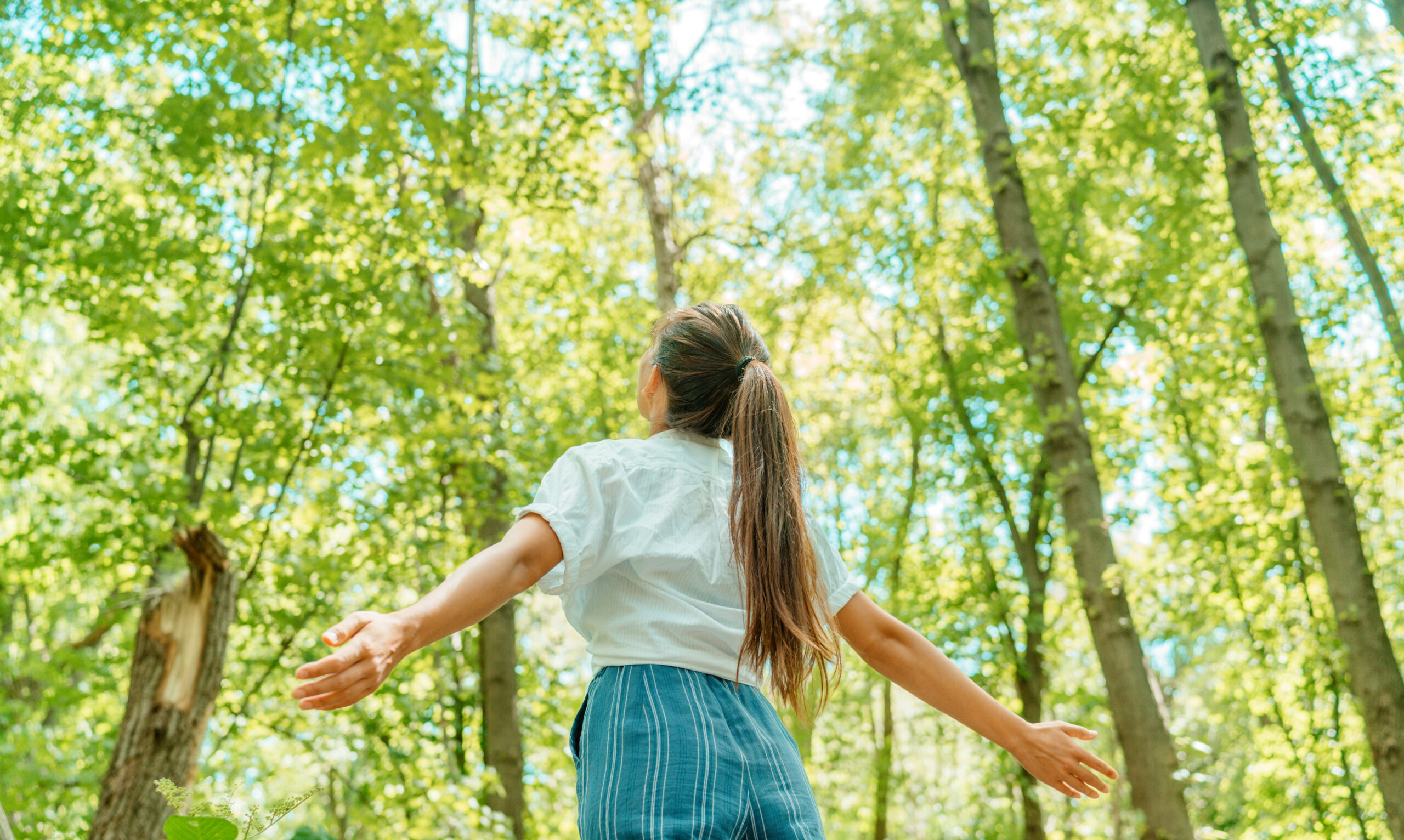 A woman walking freely through a sunlit forest with arms outstretched—capturing the refreshing link between movement and creative clarity.