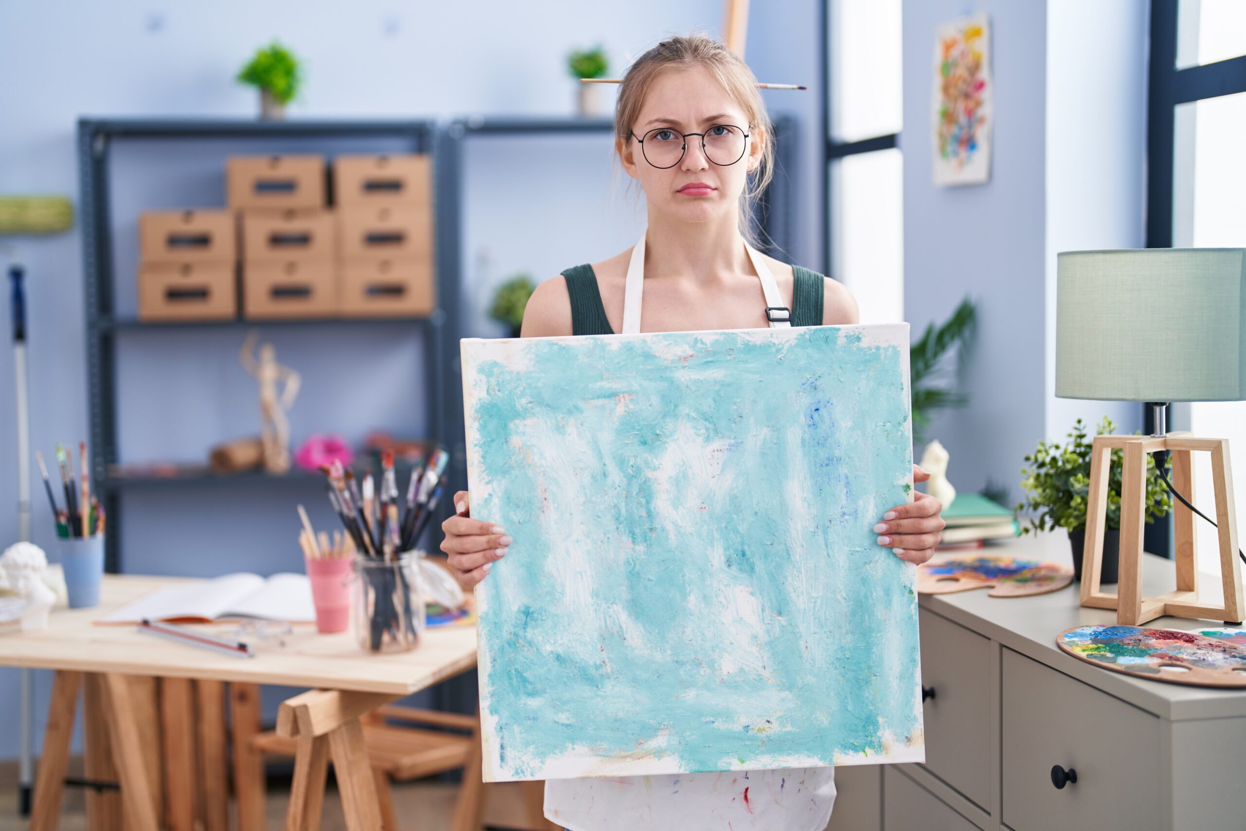 A young artist holding up an abstract painting with a playful frown—capturing the freedom and honesty of embracing imperfect art.